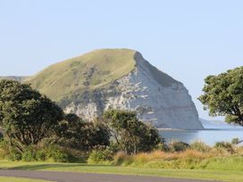A coastal landscape with a large grassy hill and trees near the shore at Sunset Haven Mahia Holiday Home Mahia Peninsula