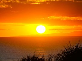 A sunset over the ocean with clouds and plants at Sunset Haven - Mahia Holiday Home Mahia Peninsula