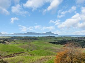 Rolling green hills with scattered trees and a body of water with mountains in the distance at Glenmohr Cabin - Waipu Holiday Retreat in Waipu