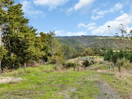A gravel and grass driveway leading through trees and fencing to a house in a rural valley with hills in the background at Glenmohr Cabin - Waipu Holiday Retreat Waipu