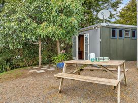 An outdoor area with a wooden picnic table set with mugs and containers next to a small building with open double doors and a satellite dish surrounded by trees at Glenmohr Cabin - Waipu Holiday Retreat in Waipu