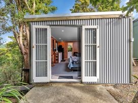 A small cabin with open glass doors showing a bed kitchen and seating area at Glenmohr Cabin - Waipu Holiday Retreat in Waipu