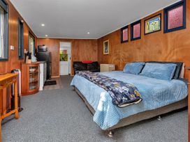 A bedroom with a large bed a black sofa a black refrigerator and a kitchenette area at Glenmohr Cabin - Waipu Holiday Retreat in Waipu