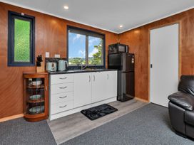 A kitchen area with white cabinets a black refrigerator a microwave a toaster and kettle next to a window at Glenmohr Cabin - Waipu Holiday Retreat Waipu
