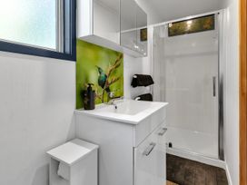 A bathroom with a white sink cabinet a wall mirror a soap dispenser a frosted window a shower with a glass door and a towel rack at Glenmohr Cabin - Waipu Holiday Retreat in Waipu