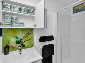 A bathroom sink with open cabinet shelves containing labeled containers and a shower with glass door at Glenmohr Cabin - Waipu Holiday Retreat in Waipu