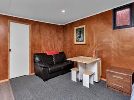 A room with wooden walls a black leather couch a folding table and stools a framed picture and a wooden cabinet at Glenmohr Cabin - Waipu Holiday Retreat in Waipu