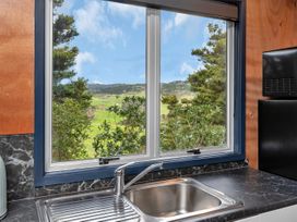 A kitchen sink with a chrome faucet under a window showing trees and hills outside at Glenmohr Cabin - Waipu Holiday Retreat Waipu