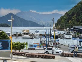 A harbor with boats docked near a pier and people standing by cars with mountains in the background at Picton Central - Picton Holiday Home