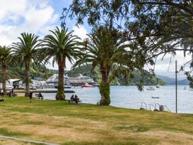 A waterfront park with palm trees benches people a large cruise ship and boats on the water at Picton Central in Picton