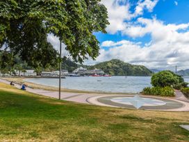 A waterfront park with grass and a paved walkway by the sea with boats and a cruise ship near green hills at Picton Central Picton