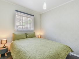 A bedroom with a bed covered in a green quilt next to two small bedside tables with lamps at Picton Central - Picton Holiday Home in Picton