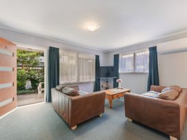 A living room with two brown leather sofas a wooden coffee table a television and windows with curtains at Picton Central Picton Holiday Home