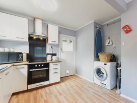A kitchen with white cabinets a stove microwave kettle and toaster next to a washing machine an ironing board and a basket at Picton Central - Picton Holiday Home in Picton