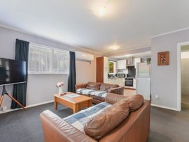 A living room with two brown leather sofas a wooden coffee table with flowers and a TV on a stand next to a window at Picton Central Picton