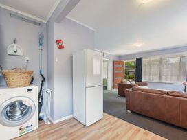 A living area with brown sofas a refrigerator a washing machine and a window with curtains at Picton Central - Picton Holiday Home