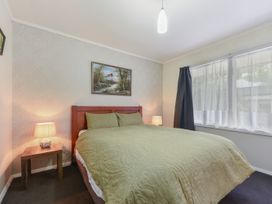 A bedroom with a bed with green bedding two bedside tables with lamps a window with curtains and a painting above the bed at Picton Central - Picton Holiday Home in Picton