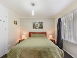 A bedroom with a bed covered in green bedding two bedside tables with lamps and a window with curtains at Picton Central - Picton Holiday Home in Picton