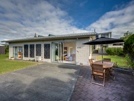 An outdoor patio area with a wooden table and chairs under a black umbrella next to a single-story house with sliding glass doors and decorative panels on the wall at Mahia Bliss - Surf & Serenity Holiday Home in Mahia Peninsula