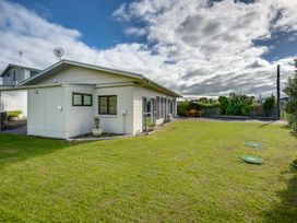 A backyard with a grassy lawn a white house with windows a wooden patio set a fence and trees at Mahia Bliss - Surf & Serenity Holiday Home in Mahia Peninsula