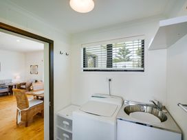A laundry room with a washing machine sink and storage next to a dining area at Mahia Bliss - Surf & Serenity Holiday Home in Mahia Peninsula