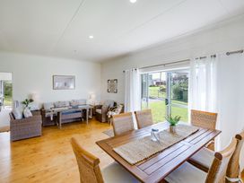 A dining area with a wooden table and chairs next to a living room with sofas and a coffee table at Mahia Bliss - Surf & Serenity Holiday Home in Mahia Peninsula