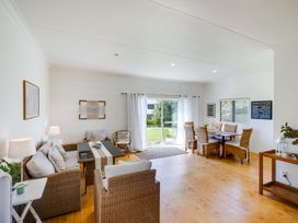 A living room with wicker furniture and a dining table near sliding glass doors at Mahia Bliss - Surf & Serenity Holiday Home in Mahia Peninsula