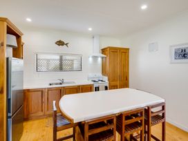 A kitchen with wooden cabinets a stove a sink a refrigerator and a white island table with wooden chairs at Mahia Bliss - Surf & Serenity Holiday Home in Mahia Peninsula