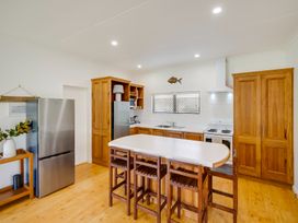 A kitchen with wooden cabinets a white countertop an island with wooden stools a stainless steel refrigerator and a stove at Mahia Bliss - Surf & Serenity Holiday Home in Mahia Peninsula