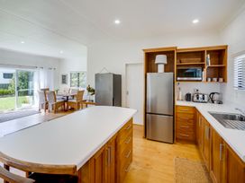 A kitchen with wooden cabinets a white countertop a dining table with chairs and sliding glass doors showing a garden at Mahia Bliss - Surf & Serenity Holiday Home in Mahia Peninsula