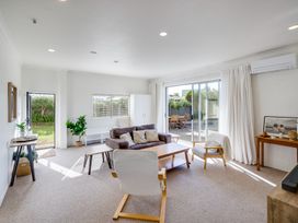 A living room with sofa chairs coffee tables and sliding doors leading to a garden at Mahia Bliss - Surf & Serenity Holiday Home in Mahia Peninsula