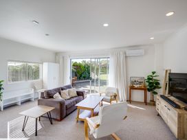 A living room with sofas chairs tables a television and sliding glass doors at Mahia Bliss - Surf & Serenity Holiday Home in Mahia Peninsula