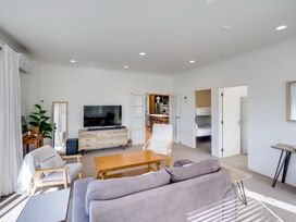A living room with a sofa chairs wooden table TV and doors leading to kitchen and bedrooms at Mahia Bliss - Surf & Serenity Holiday Home Mahia Peninsula