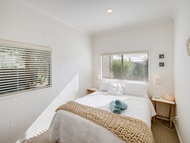 A bedroom with a bed pillows and blankets two side tables with lamps and windows with blinds at Mahia Bliss - Surf & Serenity Holiday Home in Mahia Peninsula