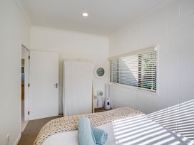 A bedroom with a bed, rolled towels, a fabric wardrobe, a small table with appliances, white blinds covering a window at Mahia Bliss - Surf & Serenity Holiday Home in Mahia Peninsula
