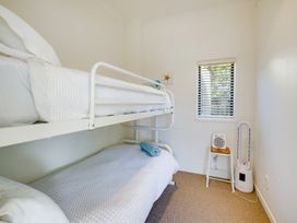A small bedroom with white bunk beds a window and a space heater on a stool at Mahia Bliss - Surf & Serenity Holiday Home in Mahia Peninsula