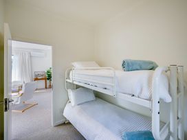 A bedroom with white bunk beds and rolled towels and a view into a living area at Mahia Bliss - Surf & Serenity Holiday Home in Mahia Peninsula