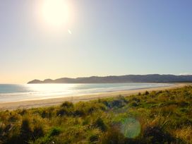 A beach with sand and grass at Mahia Bliss - Surf & Serenity Holiday Home Mahia Peninsula