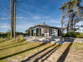 A small modern cabin with open glass doors surrounded by trees and grass at Mahanga Dunes Retreat - Mahia Holiday Home on Mahia Peninsula