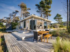 A wooden deck with outdoor furniture and folding glass doors leading to a room surrounded by trees at Mahanga Dunes Retreat - Mahia Holiday Home in Mahia Peninsula