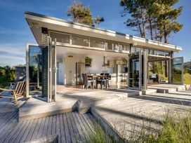 A kitchen and dining area with glass folding doors opening to a wooden deck with outdoor seating at Mahanga Dunes Retreat - Mahia Holiday Home in Mahia Peninsula