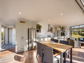 A kitchen and dining area with a wooden table and wicker chairs and stainless steel appliances at Mahanga Dunes Retreat - Mahia Holiday Home in Mahia Peninsula