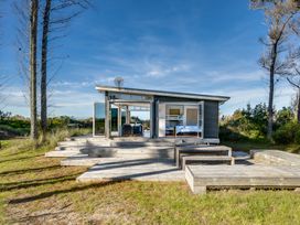 A small modern house with an open patio and wooden steps surrounded by trees at Mahanga Dunes Retreat - Mahia Holiday Home in Mahia Peninsula