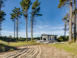 A small house with open doors and windows surrounded by tall trees and sandy ground at Mahanga Dunes Retreat Mahia Peninsula
