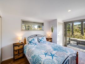 A bedroom with a bed with starfish patterned bedding two bedside tables with lamps a window above the bed and a sliding door leading outside at Mahanga Dunes Retreat - Mahia Holiday Home in Mahia Peninsula
