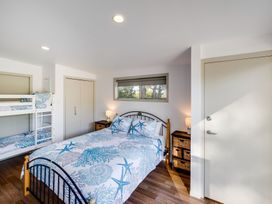 A bedroom with a queen bed and bunk beds two nightstands with lamps a window and two closets at Mahanga Dunes Retreat - Mahia Holiday Home in Mahia Peninsula