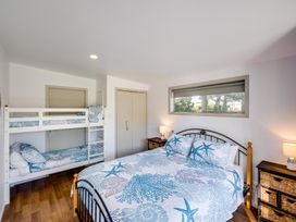 A bedroom with a double bed and bunk beds a window and nightstands with lamps at Mahanga Dunes Retreat - Mahia Holiday Home in Mahia Peninsula