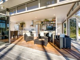 An open living room and kitchen with wicker furniture and bookshelves at Mahanga Dunes Retreat  Mahia Peninsula