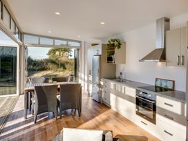 A kitchen with dining table and chairs next to large windows overlooking outdoor vegetation at Mahanga Dunes Retreat - Mahia Peninsula