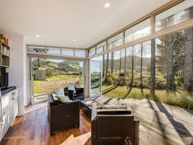 A sunroom with wicker chairs and a coffee table overlooking a wooded outdoor area at Mahanga Dunes Retreat - Mahia Holiday Home in Mahia Peninsula
